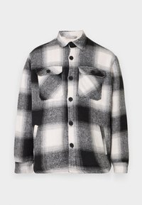 Camicia di flanella a quadri bianco e nero con maniche lunghe, bottone frontale, doppie tasche sul petto e colletto classico. Texture morbida.