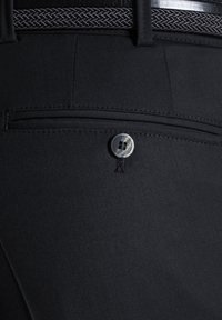 Schwarze Hose mit glatter Textur, ausgestattet mit einer Gesäßtasche und einem runden silbernen Knopf mit Rautenmuster. Akzentuiert durch einen geflochtenen Gürtel.