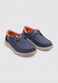 Zapatillas de lona azul marino con forro naranja, suela de goma texturada y cordones grises. Presentan costuras decorativas y un logo en el lateral.
