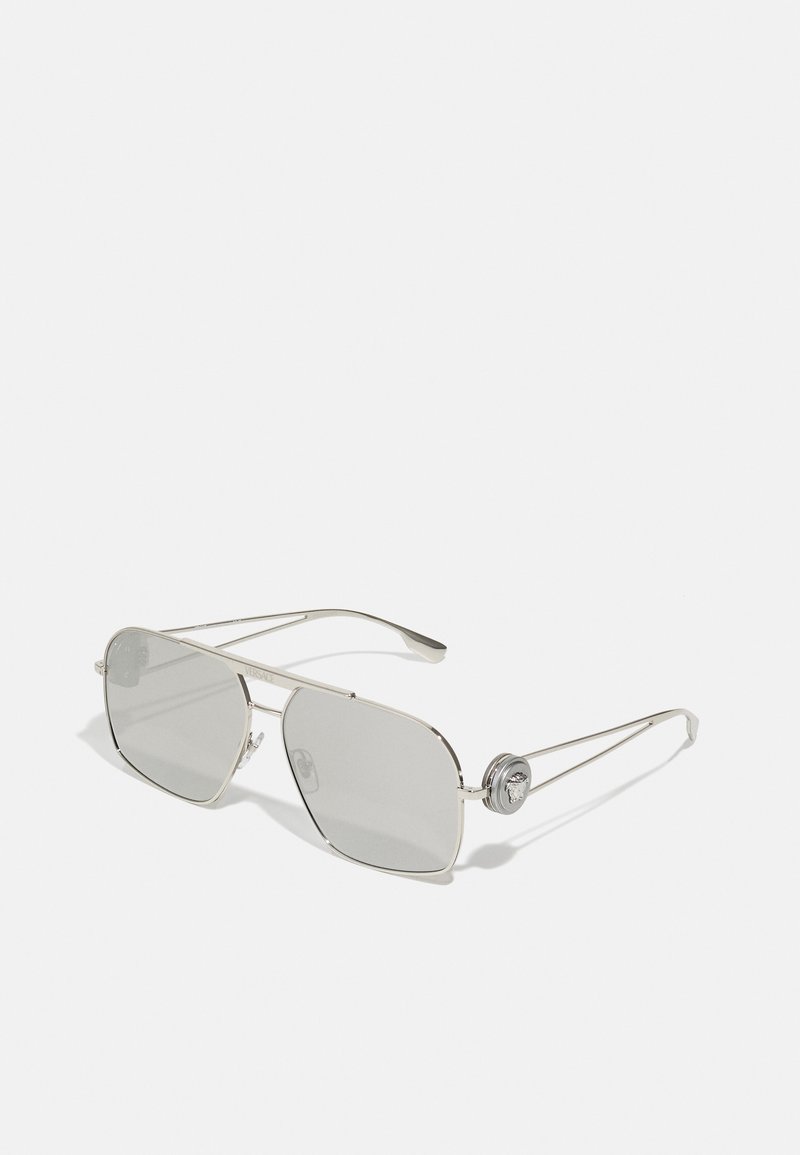 Ochelari de soare din metal argintiu cu lentile mari gri. Formă pătrată, cu un pod dublu și accente decorative ale logo-ului pe pirocheck.