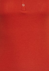 Röd ribbad tanktopp i en texturerad tygkvalitet, med en liten knappdetalj vid kragen och en figurnära passform.