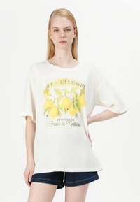 T-shirt en coton blanc oversized avec un imprimé de citrons jaunes et le texte "LES CITRONS Lérogonade Frais et Naturel." Manches courtes, coupe décontractée.