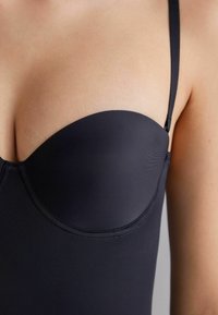 Černé spodní prádlo s hladkým materiálem, tvarovanými košíčky a nastavovacími ramínky. Obsahuje šev na spodní části pro konturování.