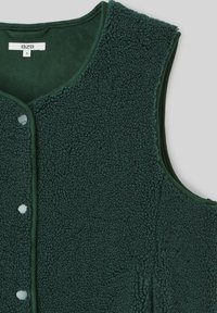 Gilet sans manches en polaire vert foncé avec des boutons pression et une petite étiquette BZB taille S à l'intérieur du col.