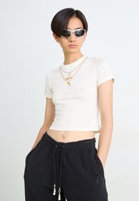 White cropped t-shirt with a gold "Jordan" print, paired with black sweatpants featuring decorative pearl accents and an elastic waistband.