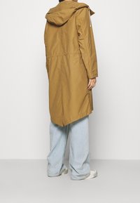 Brązowy płaszcz z kapturem, z taliowaniem, długimi rękawami i asymetrycznym dołem. Noszony na jasnoniebieskich szerokich spodniach i białych butach.