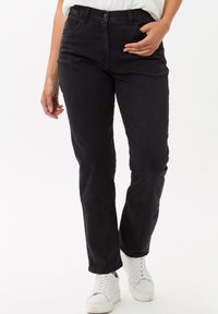 Jeans in denim blu scuro con taglio dritto, dotati di zip, cinque tasche e dettagli di cucitura frontale sottili. Abbinati a sneakers bianche.
