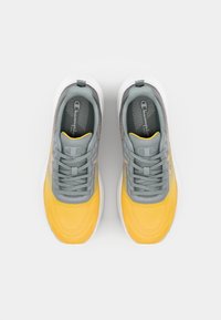 Sportieve schoenen met een grijze bovenkant, gele textuur aan de voorkant en een witte zool. Bevat veters en een patroon in de binnenvoering.