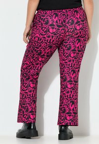 Roze broek met een patroon van zwarte cartoongezichten en symbolen, met een uitlopende snit, gecombineerd met zwarte platformboots.
