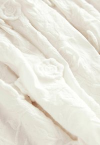 Geborduurd wit stof met textuur en bloemmotieven, zachte oppervlakte en vloeiende val, geschikt voor kleding of woningdecoratie.