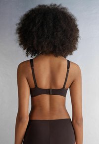 Hnědá podprsenka s nastavitelnými ramínky, hladkým povrchem, širokým pásem a háčkovým zapínáním na zadní straně. Jednoduchý design, bez vzorů či ozdob.