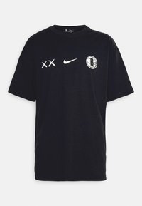 Camiseta de algodón negra con cuello redondo. Presenta gráficos blancos que incluyen "XX", el logo de Nike y un logo de baloncesto con una "B".