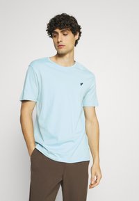 Tricou scurt cu mânecă, de culoare albastru deschis, dintr-un material moale, având guler rotund și un mic logo albastru închis pe pieptul stâng. Design simplu.