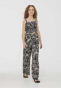 Top corto floreale bianco e nero con arricciature; abbinato a pantaloni larghi coordinati con un motivo simile. Tessuto leggero, design casual.