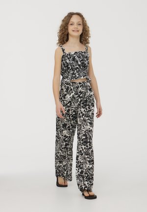 Top corto floreale bianco e nero con arricciature; abbinato a pantaloni larghi coordinati con un motivo simile. Tessuto leggero, design casual.
