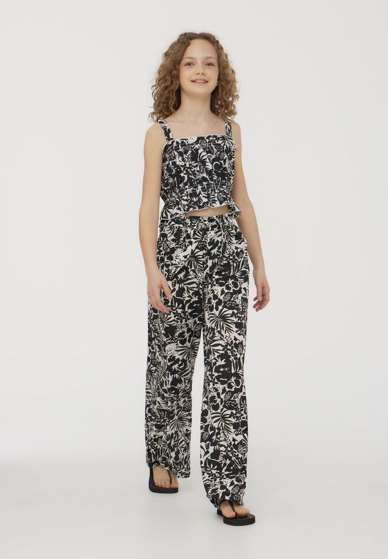 Top corto floreale bianco e nero con arricciature; abbinato a pantaloni larghi coordinati con un motivo simile. Tessuto leggero, design casual.