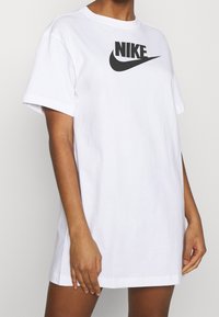 T-shirt bianco in cotone con collo rotondo e maniche corte. Presenta un grande logo Nike nero centrato sul davanti. Texture liscia.