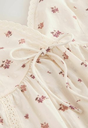 Tissu de robe couleur crème avec petit imprimé floral violet, bordure en dentelle et nœud noué à la taille.