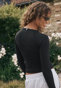 Zwarte top met lange mouwen en geribbelde textuur, aansluitend model en ronde halslijn, gecombineerd met lichtgrijze sweatpants. Zacht materiaal met een label aan de achterkant.