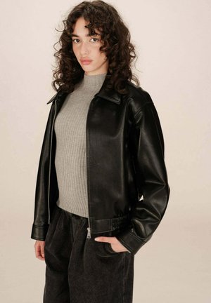 Veste en cuir noir avec fermeture éclair à l'avant, col et poignets côtelés. Associée à un pull gris à côtes et un pantalon texturé sombre.