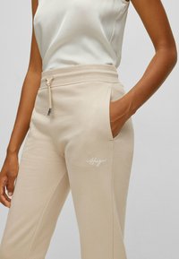 Beige Sweatpants mit einem Kordelzugbund, Seitentaschen und gesticktem Logodetail. Weicher Stoff und lockere Passform.