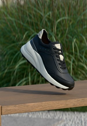 Sneaker in pelle nera con dettagli grigio chiaro, texture liscia, punta arrotondata, design con lacci e piccoli borchietti di lato.