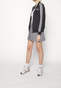 Svart zip-up jacka med vita ränder, vit crop top, svartvit rutig kjol och flerfärgade sneakers med vita detaljer.