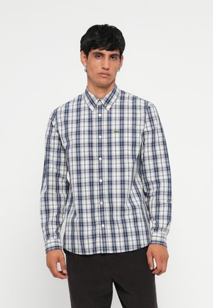 Long-sleeve button-up shirt in blue, navy, and white checked pattern. Features a collar and a small green logo on the chest pocket.