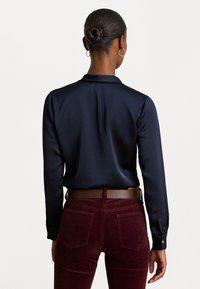 Navy satijnen shirt met lange mouwen en een kraag, gecombineerd met bordeauxkleurige corduroy broek. Inclusief een bruine riem en subtiele achternaden.