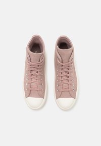 Zapatillas altas en ante rosa claro con ojales grises, puntera de goma crema y cordones a juego. Textura suave con un diseño minimalista.