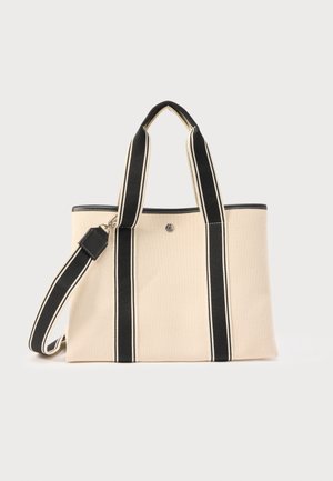 Beige lerretveske med svarte og hvite stripete håndtak og avtakbar skulderrem, med en liten rund metalllogo på forsiden.