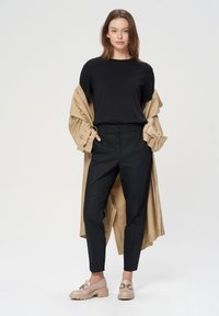 Must have lühikeste varrukatega must särk, beež trench coat üleheite, mustad kohandatud püksid ja beežid plokk-kontsaga jalanõud ketise aktsentidega. Neutraalne taust.