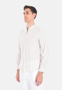 Camicia leggera con bottoni, caratterizzata da righe verticali beige e bianche, colletto alla coreana e maniche lunghe. Realizzata in tessuto traspirante.