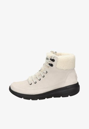 Lichtbeige suède enkellaarsjes met nep-bont kraag, zwarte rubberen zool en wit gespikkelde veters. Voorzien van een logo op de hak.