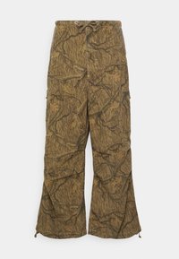 Cargo-byxor i brunt kamouflagemönster, med dragkedja i midjan, sidofickor och en avslappnad, vid bendesign. Den strukturerade tyget liknar trädbark.