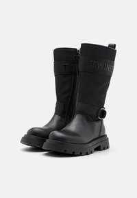 Schwarze Stiefel aus einer Kombination von Leder und Stoff, mit einer flachen Gummisohle, Reißverschluss und einem dekorativen Riemen mit der Aufschrift "TWINS."