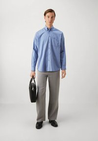 Light blue long-sleeve button-up shirt, gray trousers, black shoes, holding a black leather briefcase. Simple design, pocket detail on shirt.