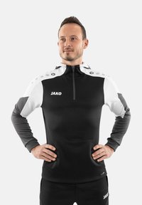 Haut de sport noir et blanc à demi-zip avec poche kangourou, logo brodé et design à pois sur les épaules. Fabriqué en tissu lisse.
