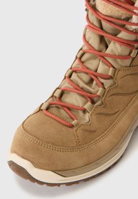 Braune Wildlederstiefel mit orangen Schnürsenkeln, gepolstertem Zungenbereich und strukturiertem Profil. Für den Außeneinsatz konzipiert, mit verstärkter Zehenkappe und flexiblem Obermaterial.