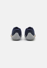 Zapatillas de trail de color azul marino con una suela gris texturizada. Presentan un diseño de caña baja, parte superior de malla y un logotipo de la marca prominente en el talón.