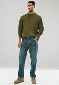 Olive green textured knit sweater, blue denim jeans, and taupe lace-up shoes. Casual outfit with a relaxed fit and subtle color contrast.