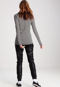 Schwarz-weißer, gestreifter Langarmoberteil, kombiniert mit schwarzen, glänzenden Jogginghosen. Verfügt über elastische Bündchen und eine elegante, schlanke Silhouette.