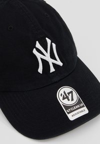 Black baseball cap made of cotton with white embroidered "NY" logo. Features adjustable strap and branded tag on the visor.