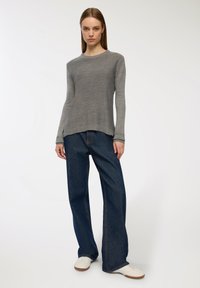 Szary sweter z długim rękawem i okrągłym dekoltem, w zestawie z niebieskimi, szerokimi spodniami z wysokim stanem i białymi trampkami na neutralnym tle.