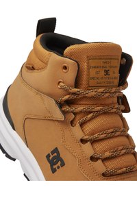 Zapatillas altas en color marrón con acabado de tela texturizada, acentos en negro, logo prominente y cordones con patrón. Presentan un cuello acolchado para mayor comodidad.
