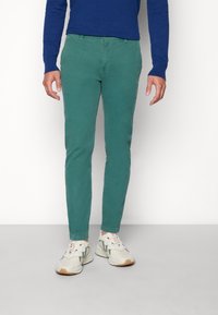 Zielone spodnie slim-fit wykonane z bawełny o gładkiej fakturze. W zestawie z białymi trampkami z szarymi i pomarańczowymi akcentami.