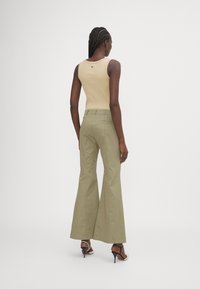 Un débardeur côtelé marron associé à un pantalon évasé vert clair, présentant une coupe slim avec des poches arrière et des talons hauts, vu de l'arrière.