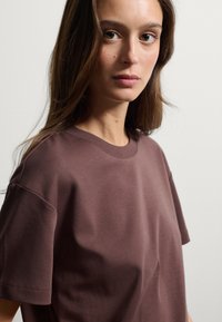 T-shirt in cotone marrone con colletto a giro e maniche corte, caratterizzato da una texture liscia e una vestibilità comoda.