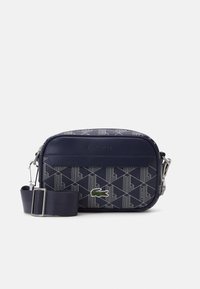 Sötétkék crossbody táska, geometrikus mintával, szintetikus anyagból, állítható pánttal és zöld Lacoste logóval. Ezüst színű fém részletek.