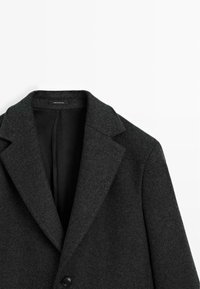 Cappotto di lana grigio scuro con rever a punta, chiusura a un bottone e foderato di nero, etichettato "made in Portugal".